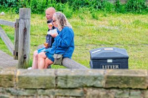 Two people sitting and eating on a bench near Litter bin