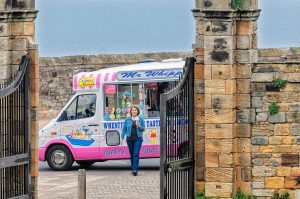 Ice cream truck near stone gate with woman and ice cream