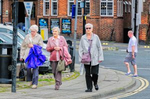 Four elderly women walking together. Man in summer clothes walks behind them.