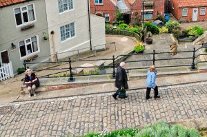 People walking on a cobblestone street with two sitting figures